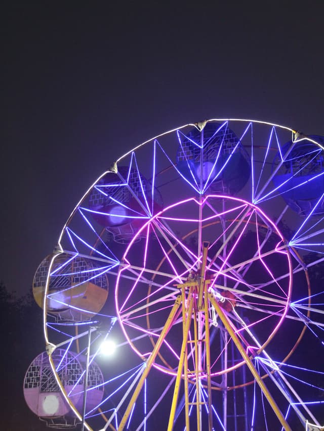A Ferris wheel illuminated with vibrant purple and pink lights against a dark night sky