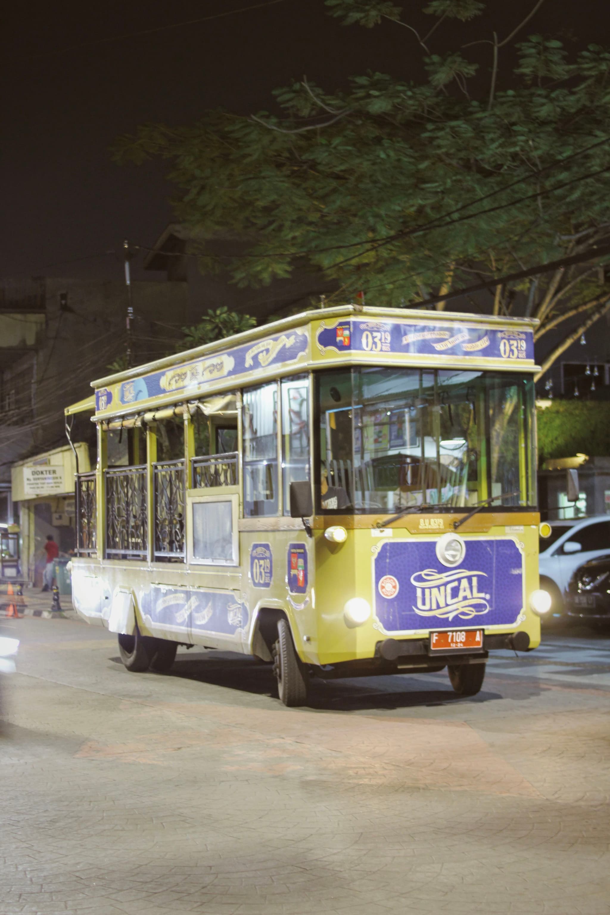 A vintage-style tram with Uncal branding is illuminated at night, traveling on a street lined with trees and parked cars