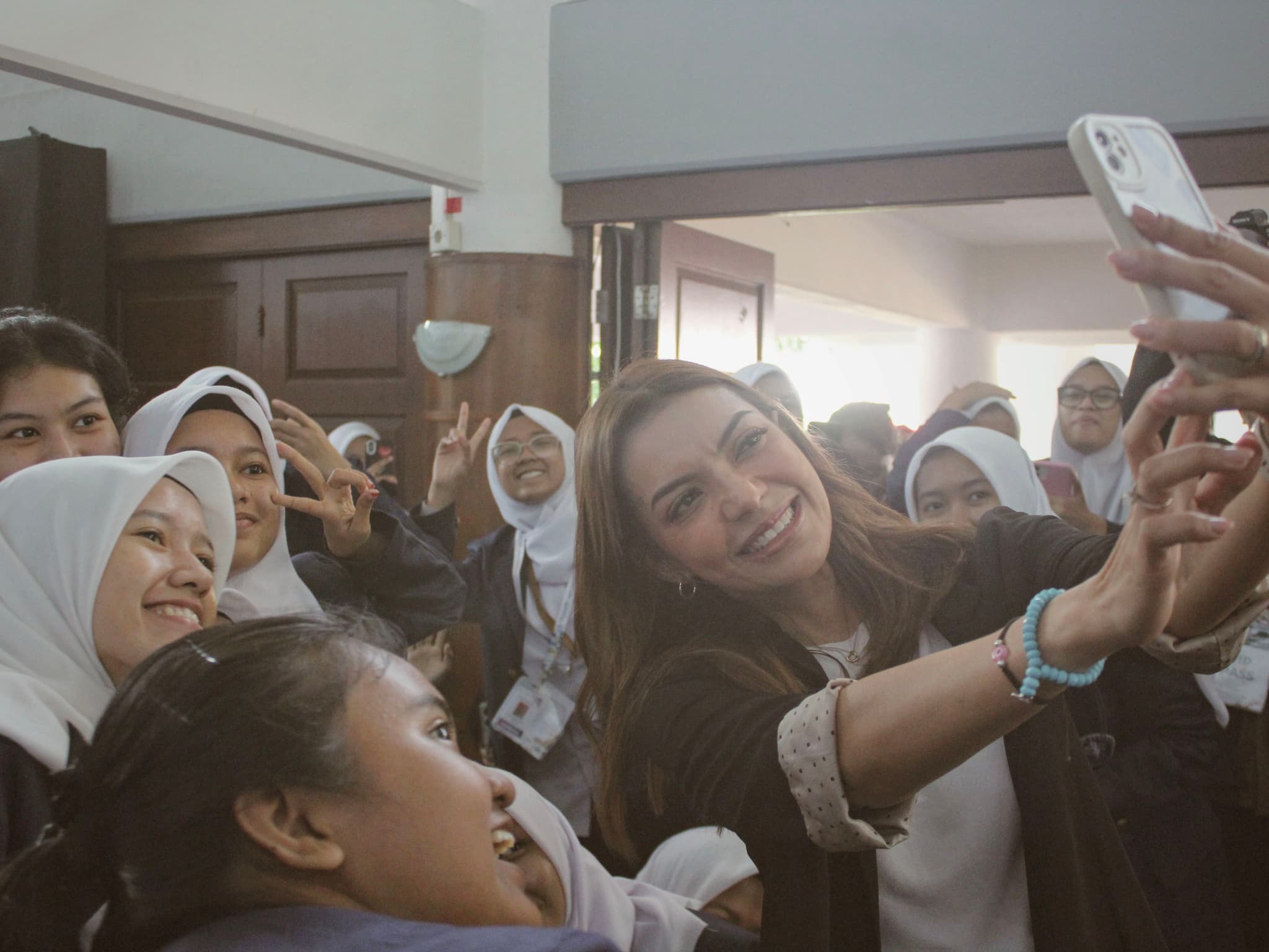A group of people, including women wearing hijabs, taking a selfie together indoors