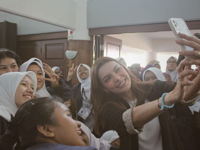 A group of people, including women wearing hijabs, taking a selfie together indoors