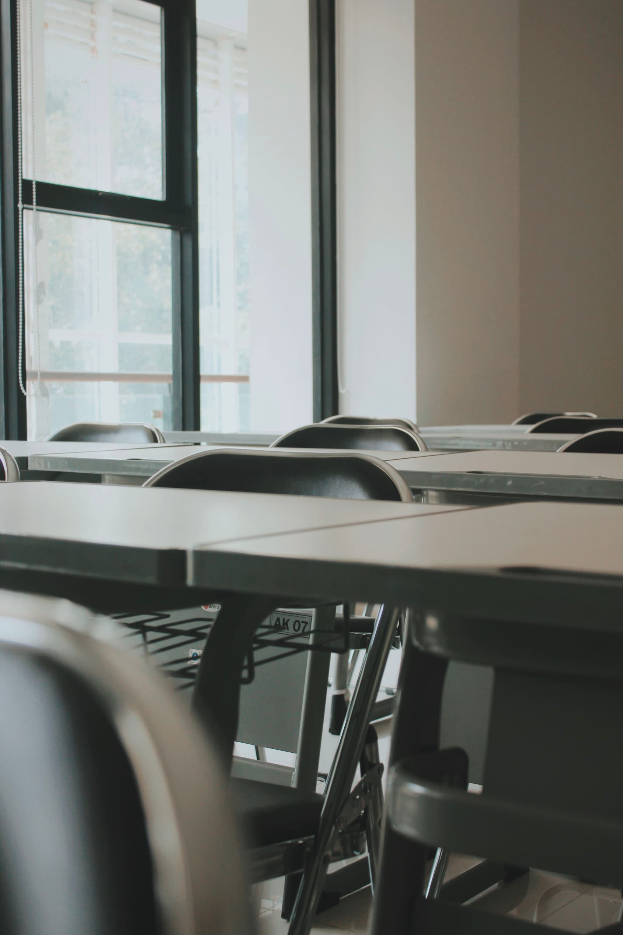 An empty classroom with rows of desks and chairs, illuminated by natural light from large windows